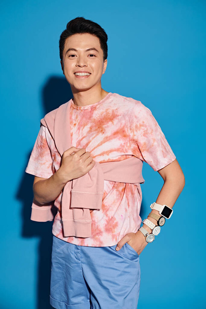 Een modieuze jongeman in trendy kleding die voor een opvallende blauwe muur poseert. - Foto, afbeelding