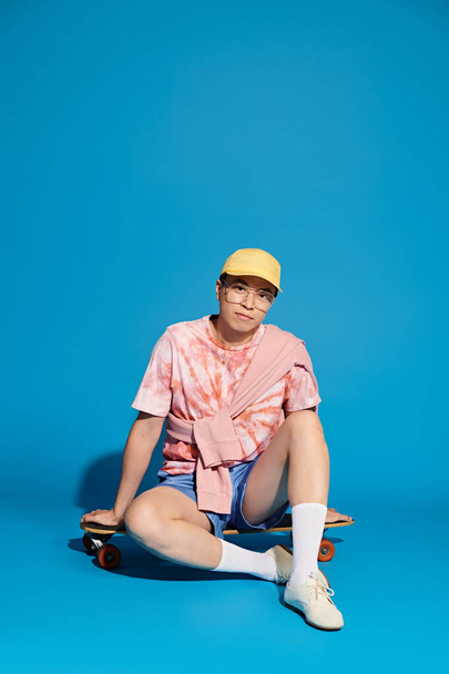 Tyylikäs nuori mies trendikkäässä puvussa istuu maassa skeittilaudalla, jossa on rentoutumisen hetki. - Valokuva, kuva