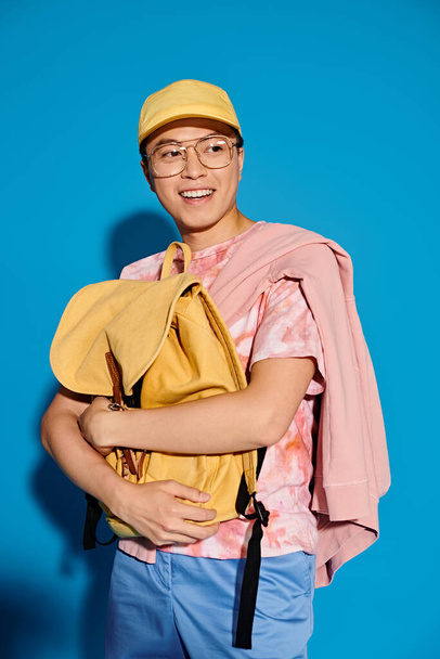 Молодий чоловік в рожевій сорочці вражає модну позу на синьому фоні, в яскравому жовтому капелюсі. - Фото, зображення
