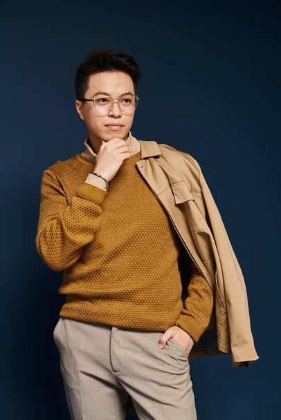 A fashionable young man in a brown sweater and glasses strikes a thoughtful pose. - Foto, Bild