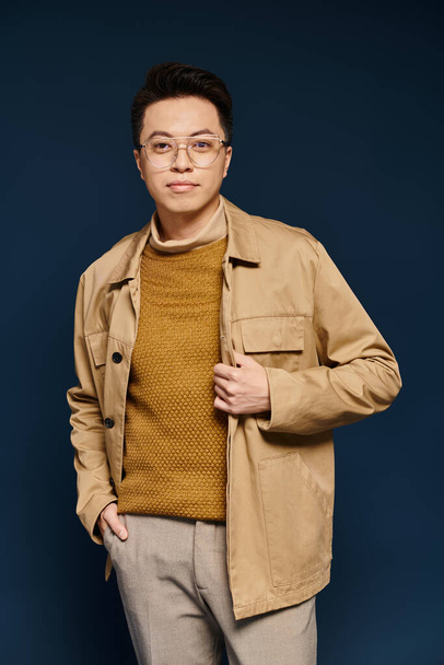 A fashionable young man confidently poses in a tan jacket and glasses, exuding elegance and charm. - Фото, изображение