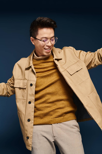 Un joven de moda en gafas y una chaqueta bronceada alcanza una pose, exudando confianza y sofisticación. - Foto, Imagen