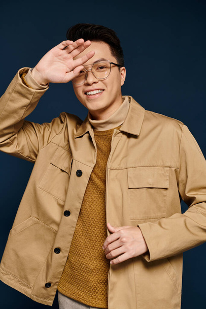 A fashionable young man with glasses poses confidently in a tan jacket, exuding elegance and sophistication. - Фото, изображение