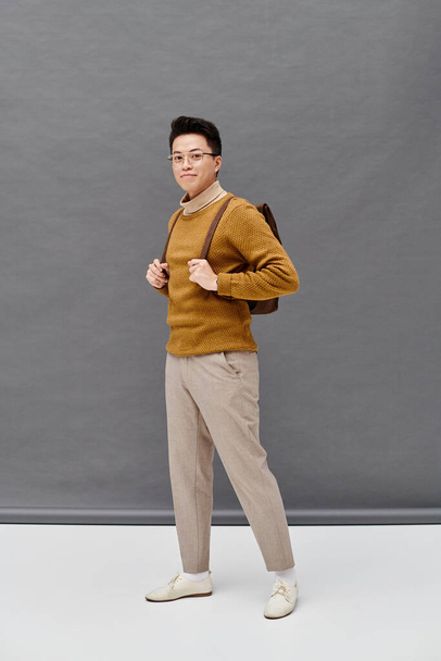 Um jovem na moda em uma camisola marrom e calças brancas golpeia uma pose dinâmica. - Foto, Imagem