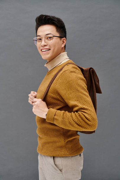 Стильный молодой человек в очках и коричневом свитере элегантно позирует. - Фото, изображение
