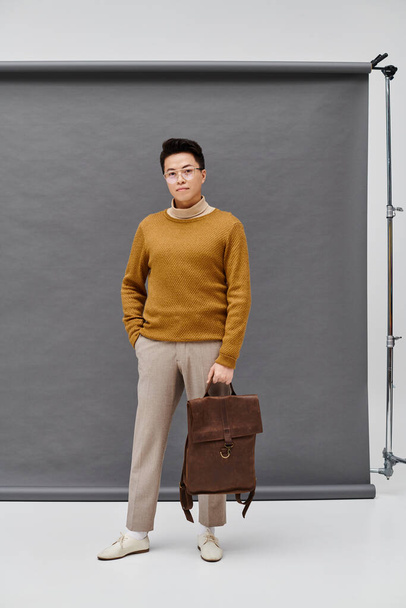 A fashionable young man stands confidently in front of a backdrop, holding a briefcase in a poised and assertive stance. - Fotografie, Obrázek