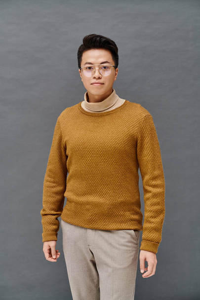 A fashionable young man in a brown sweater and tan pants poses confidently, showcasing his elegant attire. - Zdjęcie, obraz