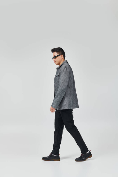 Un joven con estilo en una chaqueta gris y pantalones negros paseando con confianza. - Foto, imagen