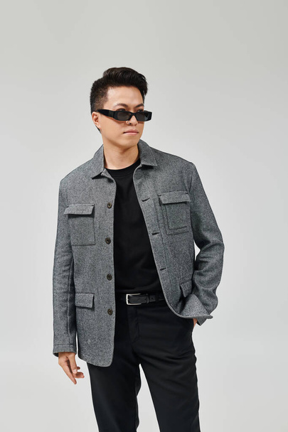 A fashionable young man strikes a confident pose in a gray jacket and black pants. - 写真・画像