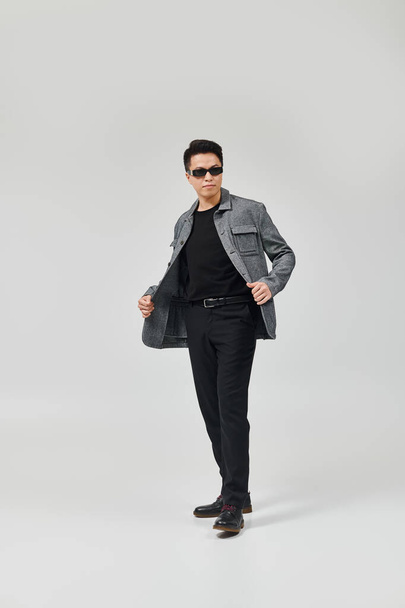A fashionable young man strikes a dynamic pose in a gray jacket and black pants. - Valokuva, kuva