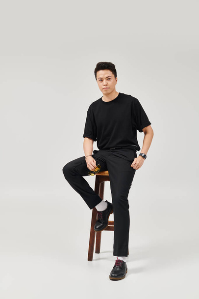 A young man in elegant attire sits on top of a wooden stool with a stylish and active pose. - 写真・画像