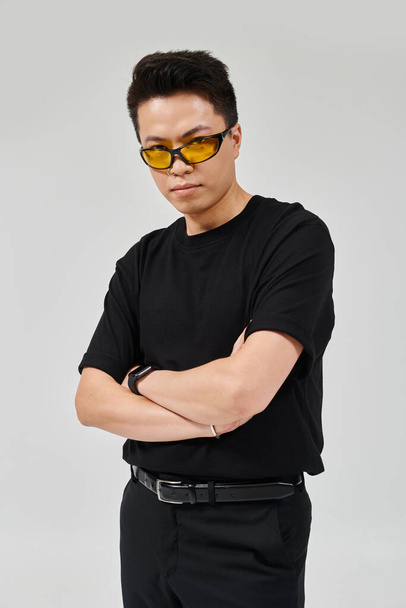 A fashionable young man with arms crossed and wearing sunglasses strikes a confident pose in elegant attire. - Foto, afbeelding