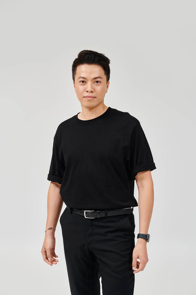 Un jeune homme à la mode pose avec confiance dans une chemise et un pantalon noirs, exsudant élégance et style. - Photo, image