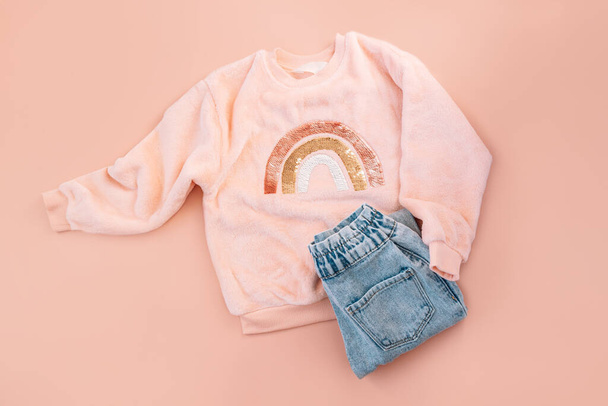 Pinkfarbener Pullover für Kinder und blaue Jeans auf rosa Hintergrund. - Foto, Bild