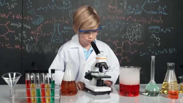 Chytrý chlapec používající vzorek mikroskopické analýzy ve vědecké laboratoři ve STEM nebo v hodině chemie. Šťastný bělošský student hledající pod dalekohledem chemickou kapalinu v tubách. Erudice. - Záběry, video