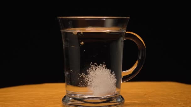 Comprimido efervescente cai em um copo de água em fundo preto e amarelo - Filmagem, Vídeo