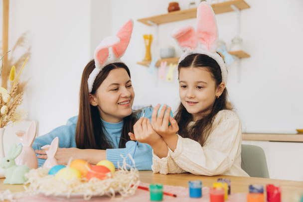 Madre e sua figlia dipingono uova. Buona famiglia che si prepara per Pasqua. Carino bambina che indossa orecchie di coniglio. - Foto, immagini