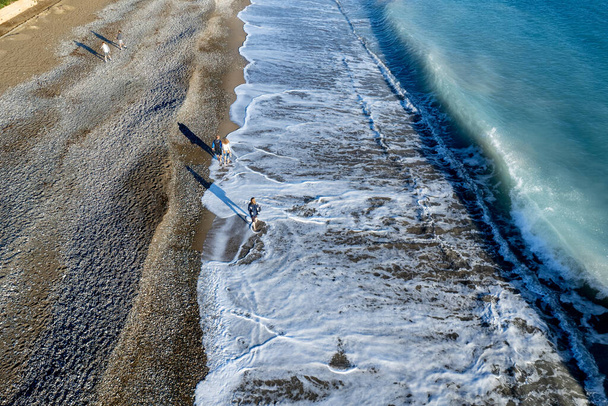 Aerial drone point of view of person walking on sand in a beach. Stormy waves idyllic beach in winter. - Φωτογραφία, εικόνα