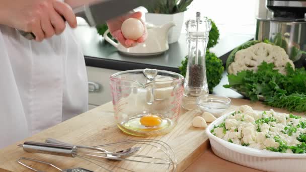Τα χέρια μιας γυναίκας σπάνε τα αυγά σε ένα ποτήρι μέτρησης, προσθέτουν ξινή κρέμα, μαύρο πιπέρι, αλάτι, σκόρδο και ετοιμάζουν την κατσαρόλα με κουνουπίδι. Κοντινό πλάνο, πλαϊνή όψη. - Πλάνα, βίντεο