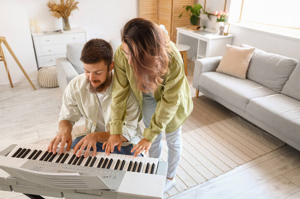 Счастливая влюбленная пара играет в синтезатор дома - Фото, изображение