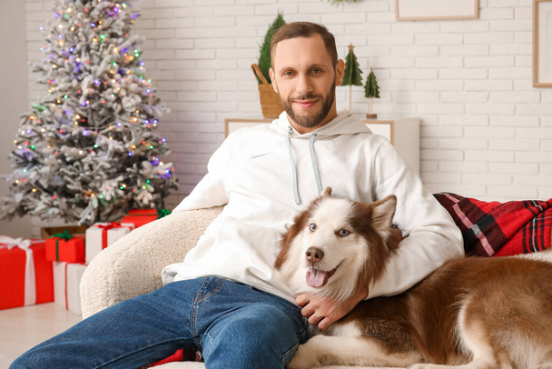 Handsome young man with cute Husky dog at home on Christmas eve - Photo, Image
