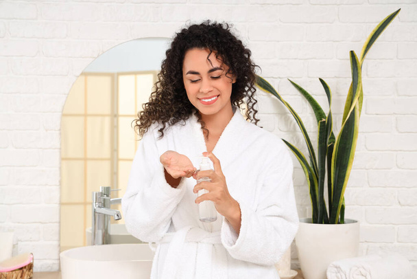 Mooie Afro-Amerikaanse vrouw met haarcrème in de badkamer - Foto, afbeelding