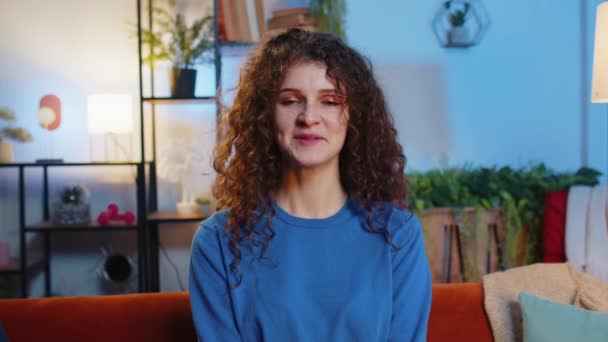 Portrait of cheerful young woman in casual clothes touching curly hair with hands sitting in living room at home. Smiling beautiful female girl playing adjusting her wavy hairstyle, looking at camera. - Footage, Video