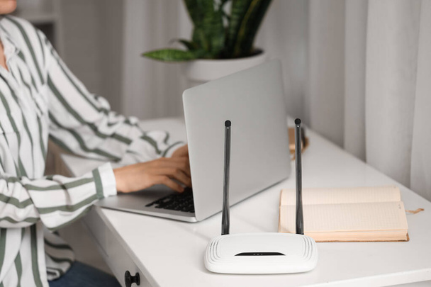 Moderne wi-fi router op tafel van werkende vrouw met laptop, close-up - Foto, afbeelding