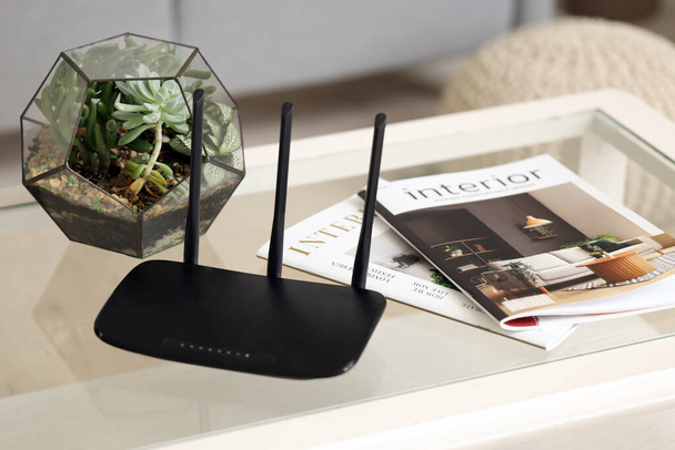 Modern wi-fi router with florarium and magazines on table in living room, closeup - Photo, Image