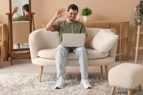 Красивий молодий чоловік використовує ноутбук, сидячи на дивані у вітальні - Фото, зображення