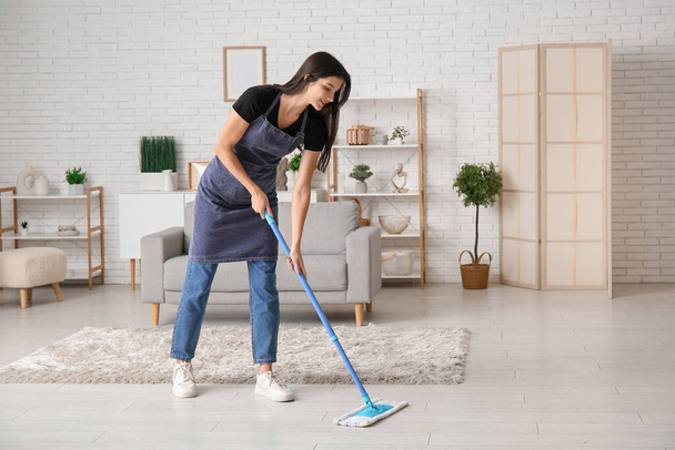 jonge vrouw dweilen de vloer in de woonkamer - Foto, afbeelding