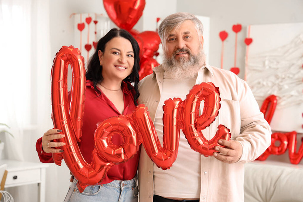 Süslü odada aşk kelimesi şeklinde balonları olan güzel, olgun bir çift. Sevgililer Günü kutlaması - Fotoğraf, Görsel
