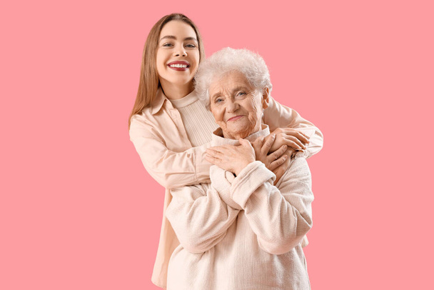 Молода жінка обіймає бабусю на рожевому фоні - Фото, зображення