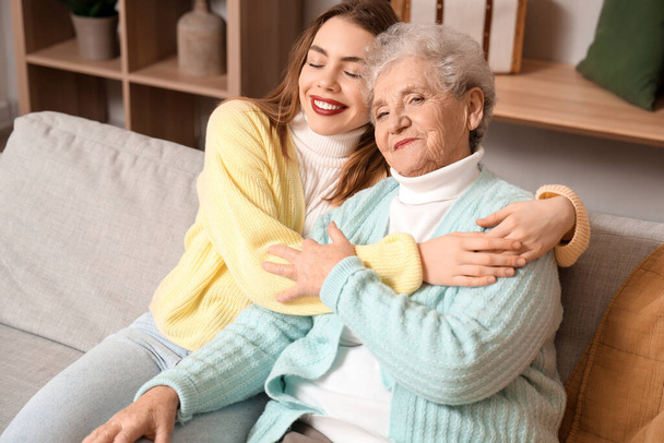 Young woman hugging her grandmother on sofa at home - Photo, Image