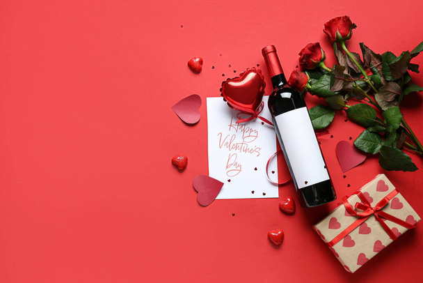Garrafa de vinho com cartão postal, rosas e presente sobre fundo vermelho. Celebração do Dia dos Namorados - Foto, Imagem