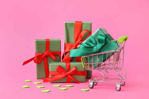 Pequeño carrito de compras con cajas de regalo sobre fondo rosa. Celebración de San Valentín - Foto, Imagen