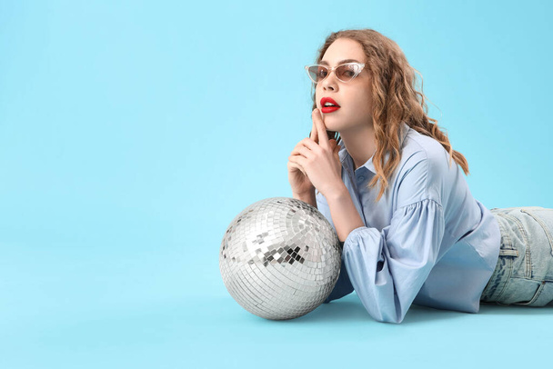 Красива молода стильна жінка з диско-кулькою лежить на синьому фоні - Фото, зображення