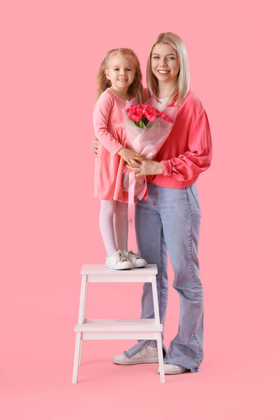 Petite fille avec des tulipes et sa mère sur fond rose. Célébration de la Journée internationale de la femme - Photo, image