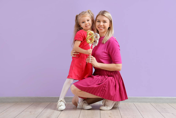 Kleines Mädchen und ihre Mutter mit Figuren 8 in der Nähe der lila Wand. Feier zum Internationalen Frauentag - Foto, Bild
