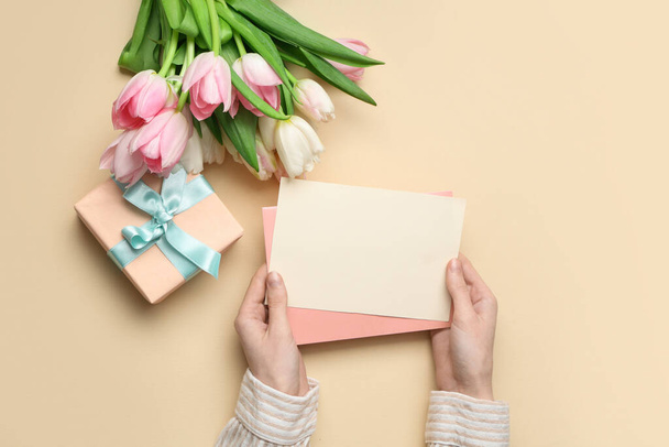 Vrouwelijke handen met blanco kaart, geschenkdoos en boeket van mooie tulpen op gele achtergrond. Internationale Vrouwendag - Foto, afbeelding
