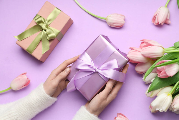 Жіночі руки з подарунковими коробками та красивими тюльпанами на фіолетовому тлі. Міжнародний жіночий день - Фото, зображення