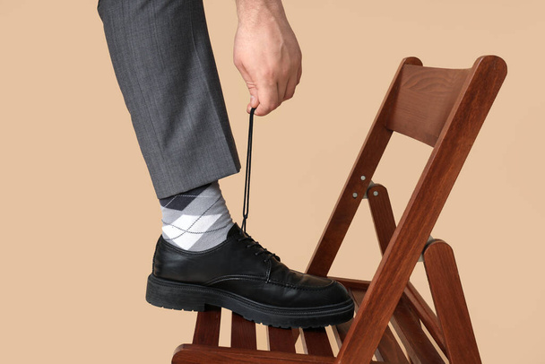 Bein eines jungen Mannes in schwarzen eleganten Schuhen auf braunem Hintergrund - Foto, Bild