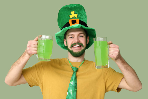 Щасливий молодий чоловік у шапці з зеленою бородою тримає келихи пива на зеленому фоні. Святкування Дня святого Патріка - Фото, зображення