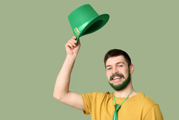 Yeşil sakallı genç adam yeşil arka planda leprikon şapka tutuyor. Aziz Patrick Günü kutlaması - Fotoğraf, Görsel