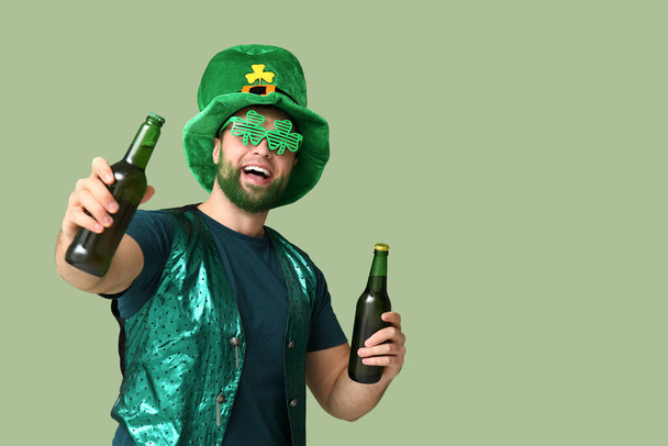 Молодий чоловік в шапці лепречуна і декоративні окуляри у формі конюшини з зеленою бородою, що тримає пляшки пива на зеленому фоні. Святкування Дня святого Патріка - Фото, зображення
