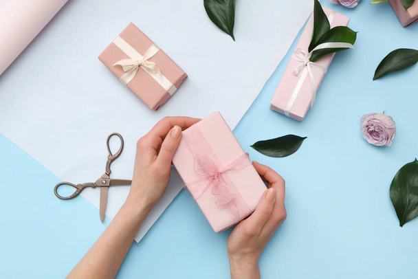 Manos femeninas con cajas de regalo, papel de regalo, hermosa rosa y hojas sobre fondo azul. Día Internacional de la Mujer - Foto, Imagen