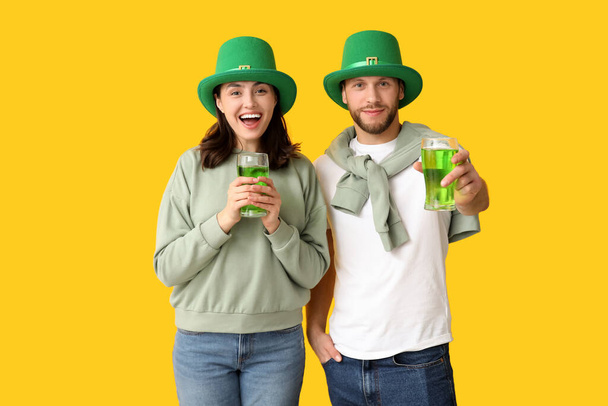 Gelukkig jong stel met kabouter hoeden met een glas bier op gele achtergrond. St. Patrick 's Day viering - Foto, afbeelding