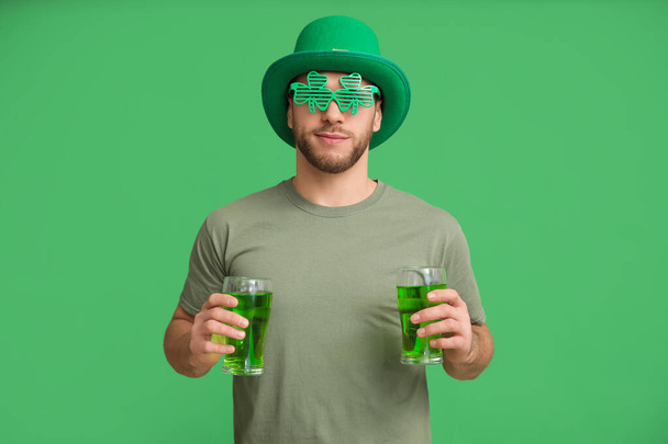 Νεαρός άνδρας με καλικάντζαρο καπέλο με ποτήρια μπύρας σε πράσινο φόντο. Γιορτή του Αγίου Πατρικίου - Φωτογραφία, εικόνα