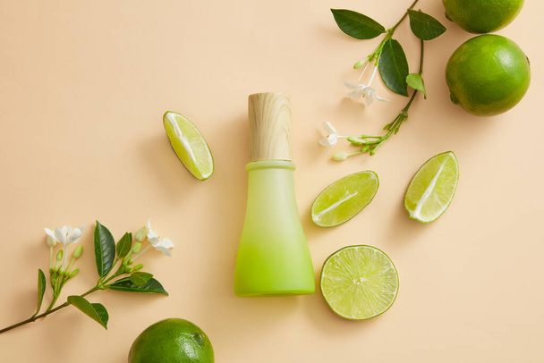 Flower branches with Limes and Lime slices are displayed with an unlabeled jar. The citric acid of Lime (Citrus aurantiifolia) gradually fades spots and evens out skin tone - Photo, Image