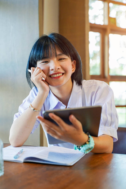 Primer plano y vista frontal de la felicidad alegre estudiante tailandesa sosteniendo una tableta con el estudio en el aula en el fondo de la bengala del sol. Concepto de educación en red. - Foto, Imagen
